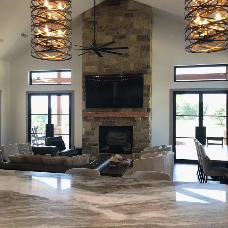 Living room with a stone fireplace, tall windows and large iron light fixtures