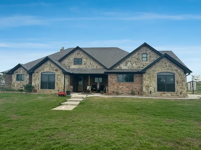 The finished Lake Kiowa home, a single-story stone and brick house with a dark roof and a green front lawn